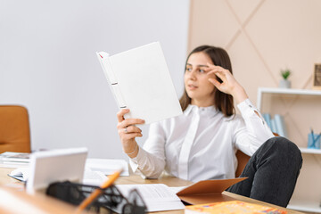 The smiling woman holding an open book in her hands and sitting at the table
