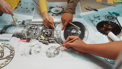 Engaged hands of a diverse team discussing and analyzing detailed technical drawings of turbine...