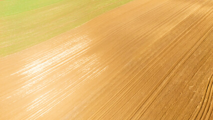 Aerial view of farm fields showcasing contrasting colors of green and golden brown soil. The lines of tillage create a rhythmic pattern under bright sunlight, emphasizing agricultural landscape beaut