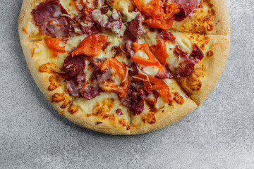 Delicious pizza topped with meats and vegetables on a gray surface