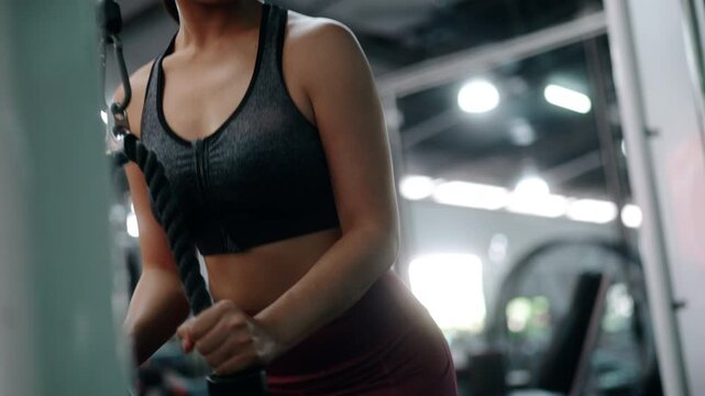 Determined athletic woman performing intense triceps pushdown using cable ropes, showcasing strength and fitness focus during gym workout
