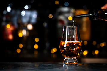 Scotch whisky pours n glencairn glass on black bar counter background