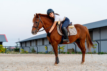 Side view of teen girl stay on the horse and bend down to make horse to relax before train or practice in the arena.