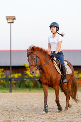 Vertical image of teen girl ride brown horse in racecourse with warm day light and she look happiness for training.