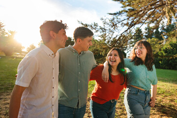 Young group of four close friends walking side by side through the park at sunset