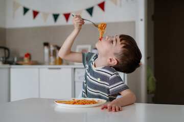 A charming boy eats spaghetti with tomato bolognese. A happy child eats freshly prepared healthy...