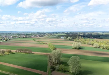 Gardinen Aerial view of lush green fields interspersed with patches of farmland under a partly cloudy sky. The landscape showcases rural serenity in springtime. © daily_creativity