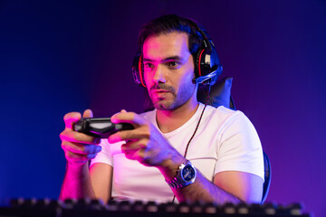 Smart gaming streamer concentrating gaming players trying to pass the level at mission completed with joystick control, talking others via mic on streaming live at neon lighting studio room. Surmise.