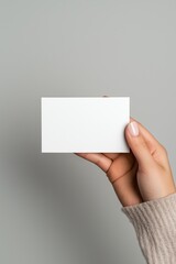 Obraz premium A hand holding a white card with no writing on it. The card is rectangular and he is made of paper