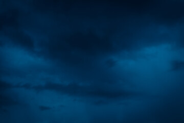Fototapeta premium Moody, dramatic storm clouds fill a deep blue evening sky, creating a mysterious and intense atmosphere. Ideal as background or for thematic visuals.