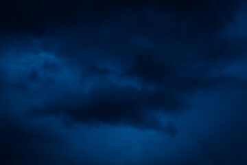 Moody, dramatic storm clouds fill a deep blue evening sky, creating a mysterious and intense...