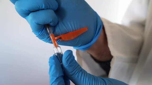 Doctor in blue gloves charges syringe with medicine from glass ampoule