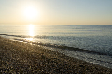Golden sunrise reflecting on calm sea waves washing pebbled beach