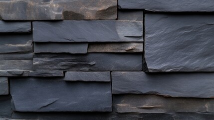 Dark gray stone wall texture.  Close-up view of interlocking rectangular stone panels in a variety of shades of dark gray, creating a modern,  rustic design