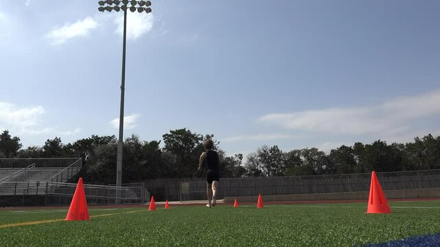 Low angle video of a young male athlete running conditioning sprints on a football field for training