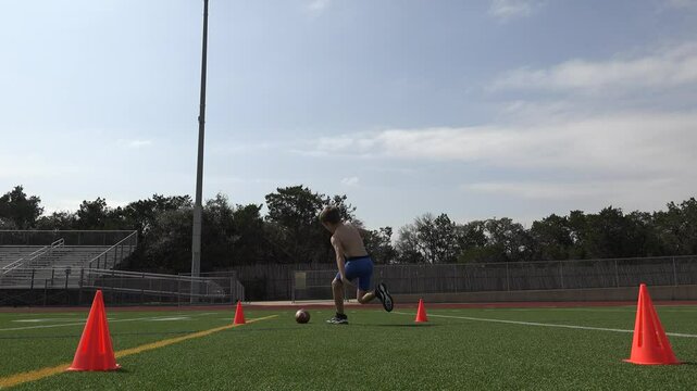 Low angle video of a shirtless young football player running conditioning sprints on a football field for training