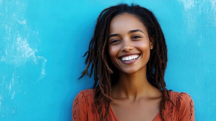A young woman with long black dreadlocks stands smiling against a light blue background.