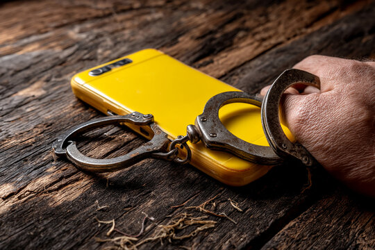 Yellow phone and handcuffs on rustic wood, depicting cybercrime or digital security issues