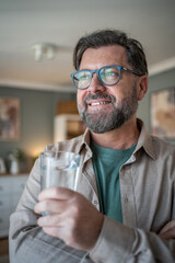 Smiling bearded man wearing glasses holding glass of water looking away