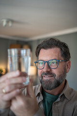 Mature man holding and observing glass of water at home