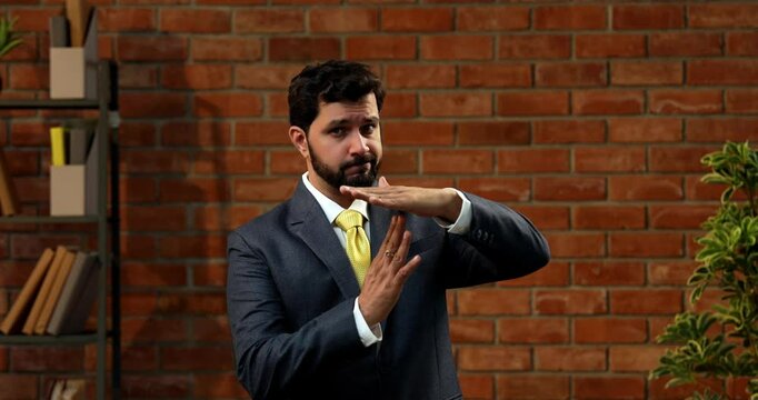 Indian businessman making take-a-break hand gesture in stylish office, Asian CEO or entrepreneur with beard suggesting pause or timeout while wearing formal suit and tie in office