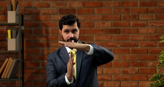Indian businessman making take-a-break hand gesture in stylish office, Asian CEO or entrepreneur with beard suggesting pause or timeout while wearing formal suit and tie in office
