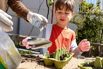 Child fills recycled egg carton with soil for seed planting under adult guidance.