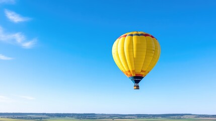 Obraz premium A bright yellow hot air balloon floats serenely in a clear blue sky above a landscape of rolling green fields