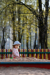 Little toddler girl sitting and playing in sandbox outdoors in park. Adorable little girl playing alone on a playground. Active child. Outdoor creative activities for kids.