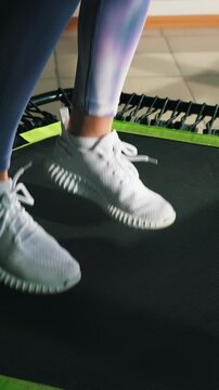 Energetic young fitness girl in blue iridescent leggings jumping on mobile mini trampoline. Close-up of legs. High intensity interval cardio training, women's health
