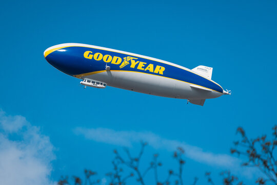 Ljubljana, Slovenia, 19.4.2025: goodyear blimp floats in a clear blue sky, with "GOODYEAR" on its side, above blurred trees, symbolizing aerial adventure and branding.