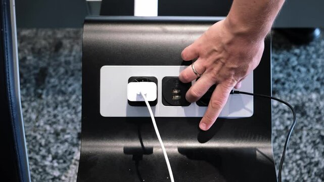 A man inserts a plug into an electrical outlet for charging his phone in a public place. Comfortable conditions for passengers in the waiting area with power sockets for plugs and USB near the seats.