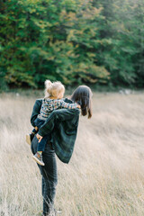 Mom corrects a little girl on her back while standing on the lawn. Side view