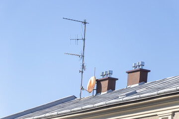 Communication antenna installed on a residential roof, featuring multiple chimneys against a clear blue sky. Represents technology in home settings.