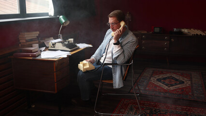 Male novelist in vintage office on phone, typewriter and scattered papers in cinematic soft-focus