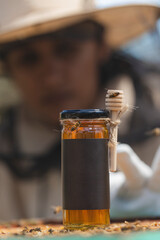 Jar of honey with dipper and bees in focus, beekeeper in background