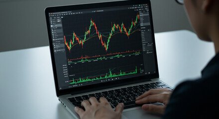 Analyzing stock market trends on laptop green and red candlestick charts dark screen focused trader