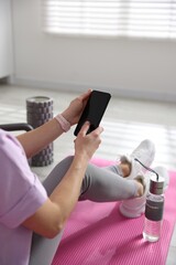 Fototapeta premium Woman with smartphone on fitness mat in gym, closeup