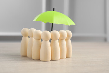 Human figures under umbrella on light wooden table. Insurance concept