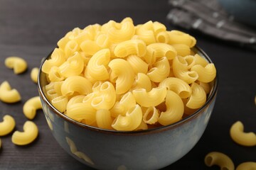 Raw horns pasta in bowl on dark table, closeup