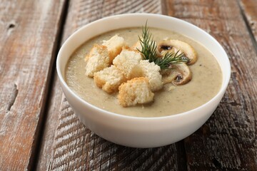 Delicious mushroom cream soup with croutons and dill on wooden table, closeup