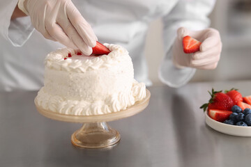 Confectioner decorating cake with strawberries at table, closeup