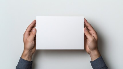 Obraz premium A person holding a blank white paper with both hands against a plain light background, professional presentation concept, and minimalistic composition.