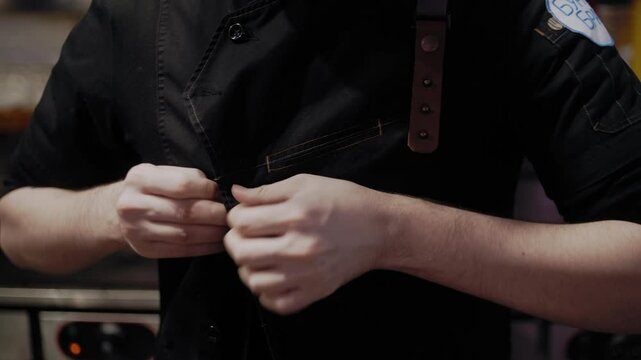 Morning kitchen routine of a chef fastening his uniform before meal prep begins.