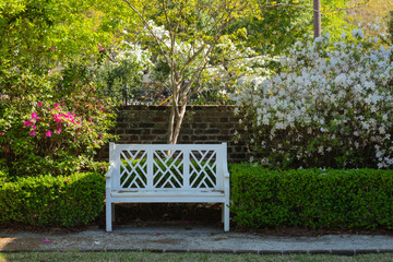A white bench sits peacefully between vibrant azaleas and lush greenery at Middleton Place, Charleston, framed by a brick wall and blooming flowers