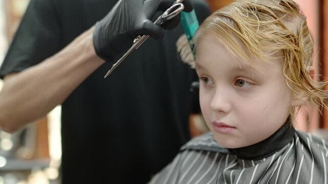 Cute school age boy getting haircut in barbershop. Children hairdresser with professional tools - comb and scissors. Cutting hair for kids. Services of a professional stylist.