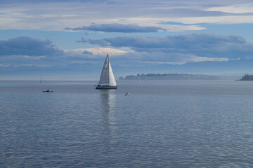 A sailboat glides across Lake Constance under a cloudy sky. The boat has a white sail and is...