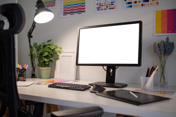 Graphic designer workspace with blank computer monitor, color palettes, graphic tablets, and creative tools.