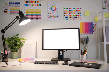 Graphic designer workspace with blank computer monitor, color palettes, graphic tablets, and...