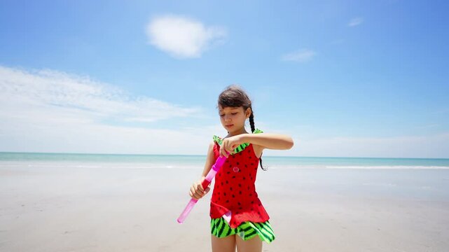 Happy Children travel playing at the sea on summer beach holiday vacation. Little cute Asian child girl kid in swimwear enjoy and fun outdoor lifestyle playing bubble wand at tropical island beach.